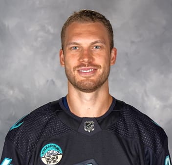 Portrait of a smiling male hockey player wearing a black team jersey with logos.